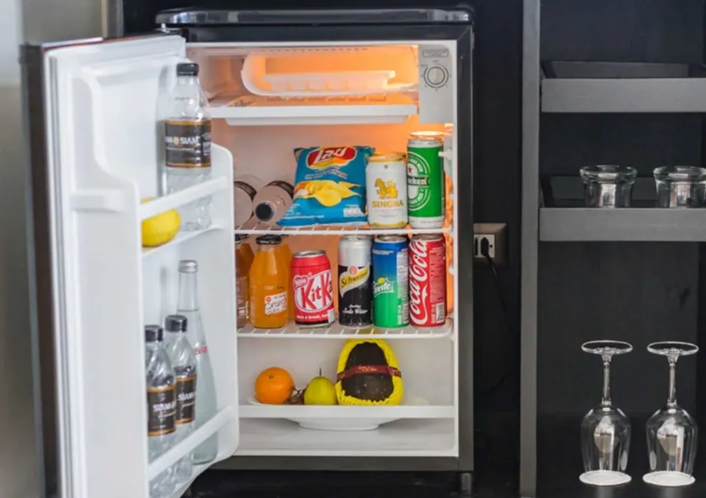 Open compact refrigerator with bottles, cans and food on the shelves